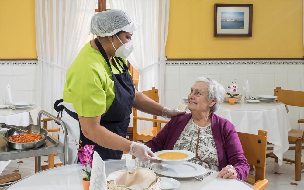 Una trabajadora de Zaintzen sirviendo la comida a una residente